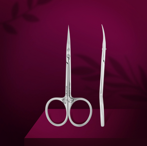 Professional cuticle scissors with curved handles and narrow tips, displayed alongside a straight edge, on a purple background with a magnolia leaf motif.