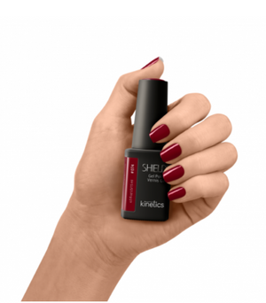 Hand holding a bottle of Kinetics nail polish with red nail polish on nails