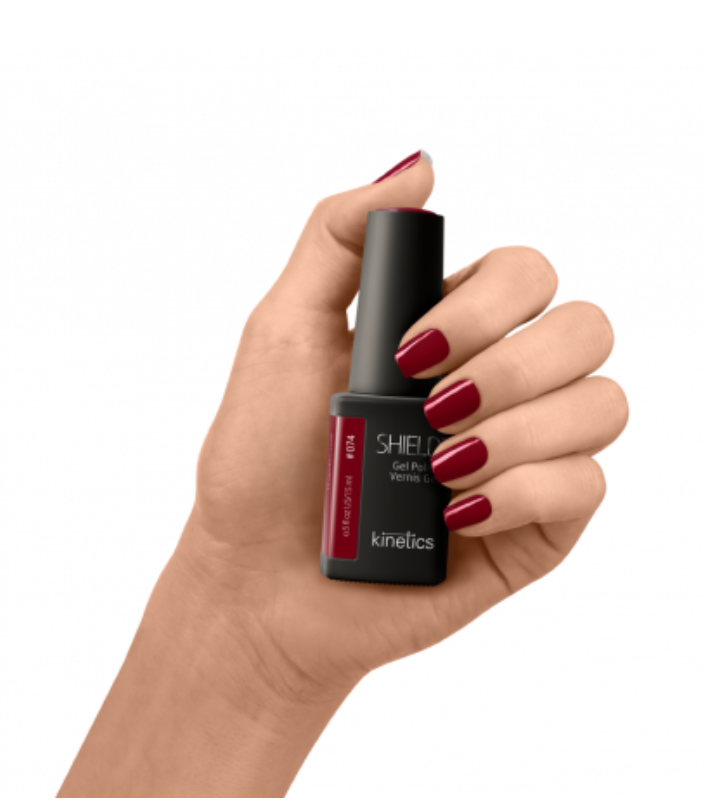 Hand holding a bottle of Kinetics nail polish with red nail polish on nails