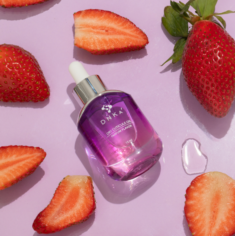 Dink'a cuticle oil dropper bottle surrounded by strawberries on a pink background