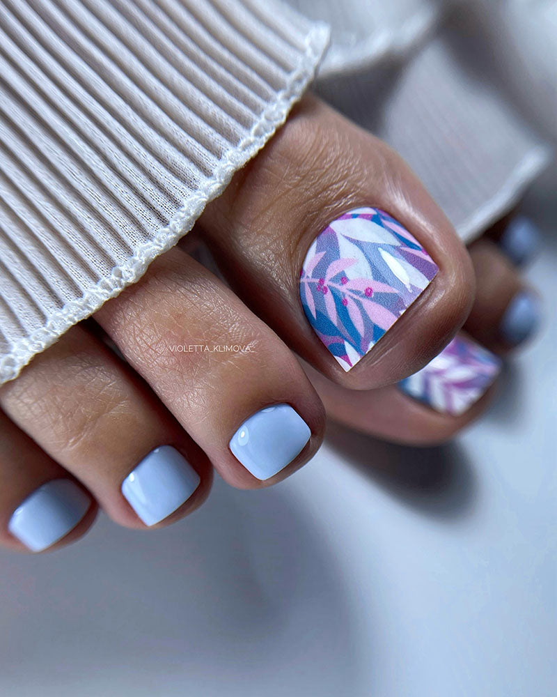 Close-up of a hand with light blue nail polish and a pink and blue floral design on one nail.