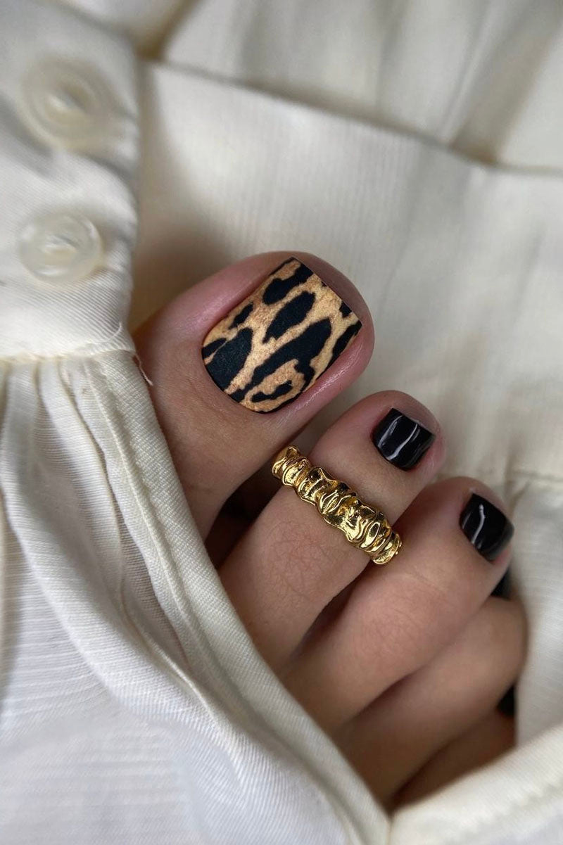 Toe with leopard print nail design and gold ring, wearing a white garment.