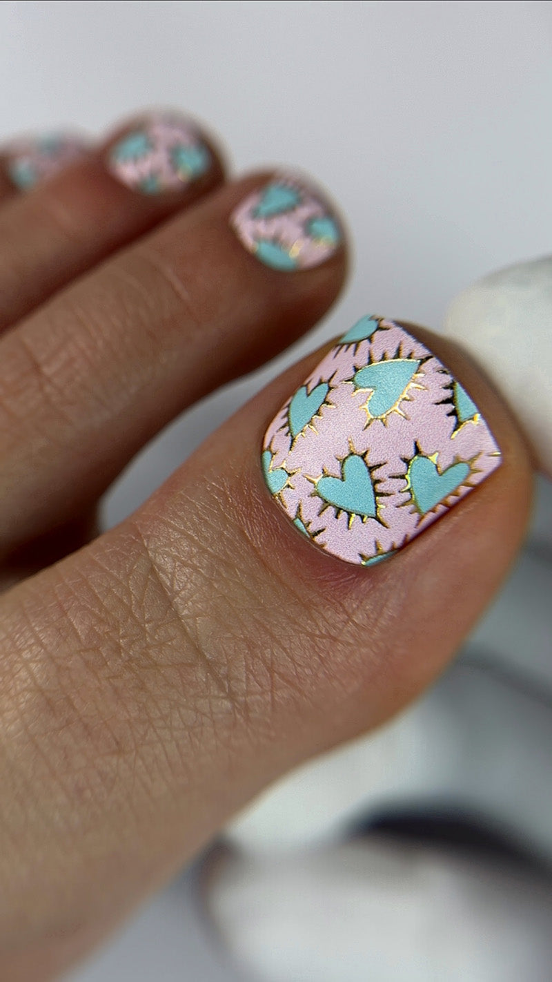 Nail art with pink and green heart designs on a neutral background