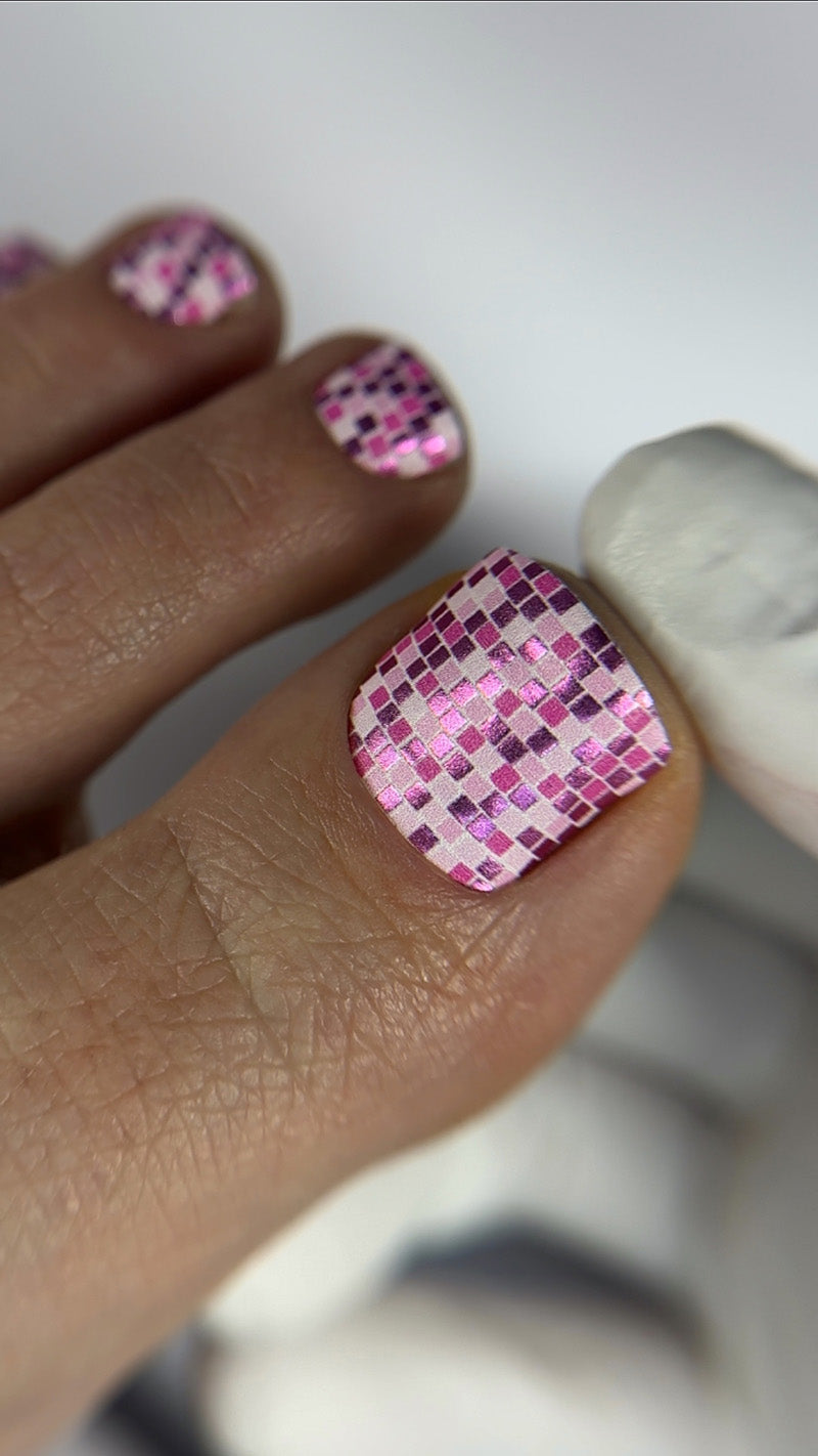 Close-up of a hand with pink and purple checkered nail design.