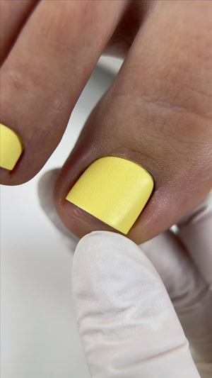 Close-up of a hand with yellow nail polish on a white background