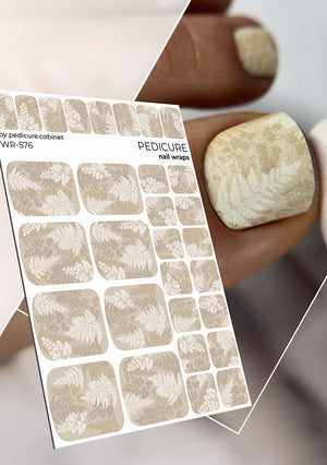 Sheet of nail wraps with a floral design held by a hand. Pedicure nail wrap nude color with leaves on white background