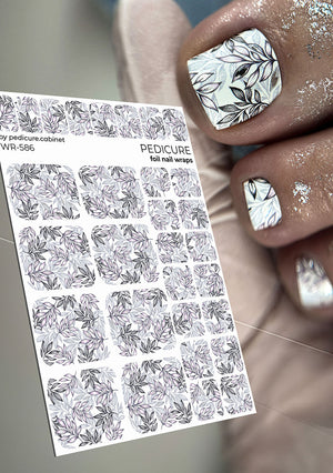 Foil pedicure nail wraps with leaf design held by a hand with similarly designed nails.
