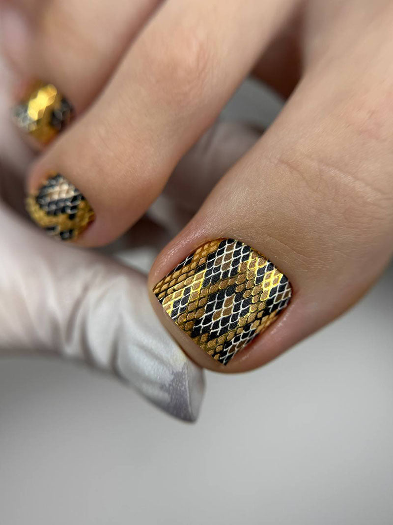 Close-up of a hand with gold and black patterned nails on a neutral background