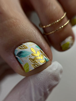 Close-up of a hand with a nail featuring gold and teal leaf design.