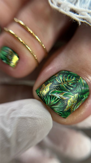 Close-up of a hand with green and gold nail art on a blurred background