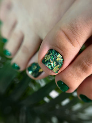 Close-up of a hand with green nail polish and a leaf design on a blurred green background