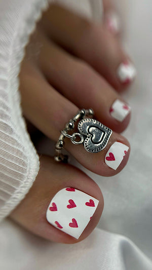 Close-up of a hand with heart-themed nail design and silver ring with heart charm.