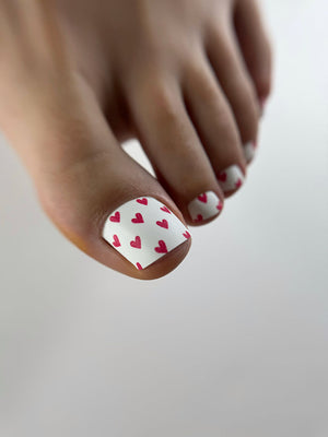 Close-up of a foot with toenails painted white and red hearts on a light background
