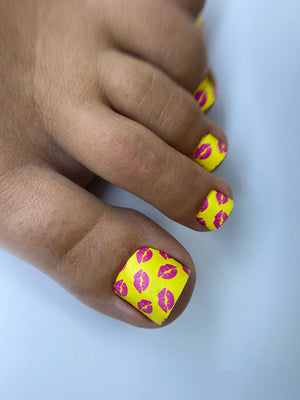 Hand with yellow nail polish featuring pink lip prints on a white background