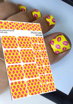 Yellow nail wraps with pink lip prints on a sheet and applied to nails.