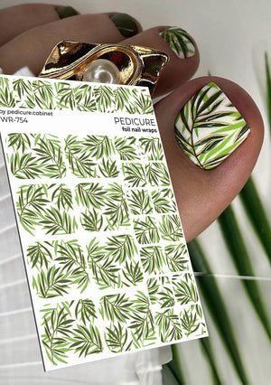 Nail wrap with green leaf pattern held by a hand with matching nail design.