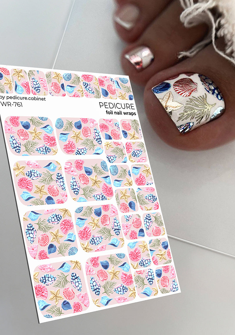 Sheet of foil nail wraps with sea-themed design next to a hand with decorated nails.