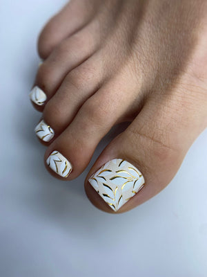 Toe nails with white nail polish and gold patterns on a light background