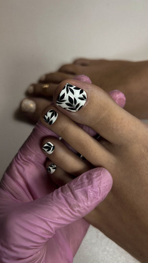 Hand with black and white patterned nail polish and ring, wearing a pink glove.