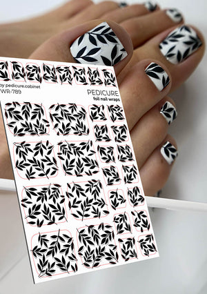Foil nail wraps with black leaf pattern held by a hand with similar nail designs.