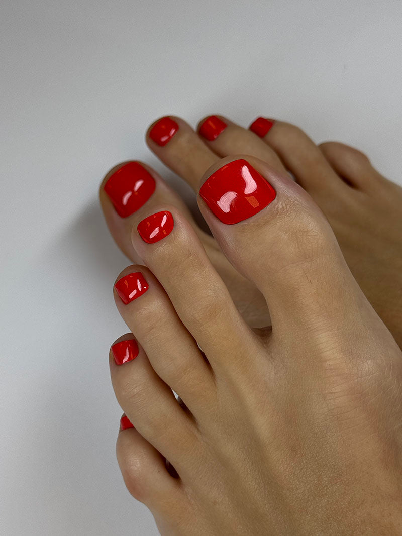 Close-up of feet with red nail polish on toes against a neutral background