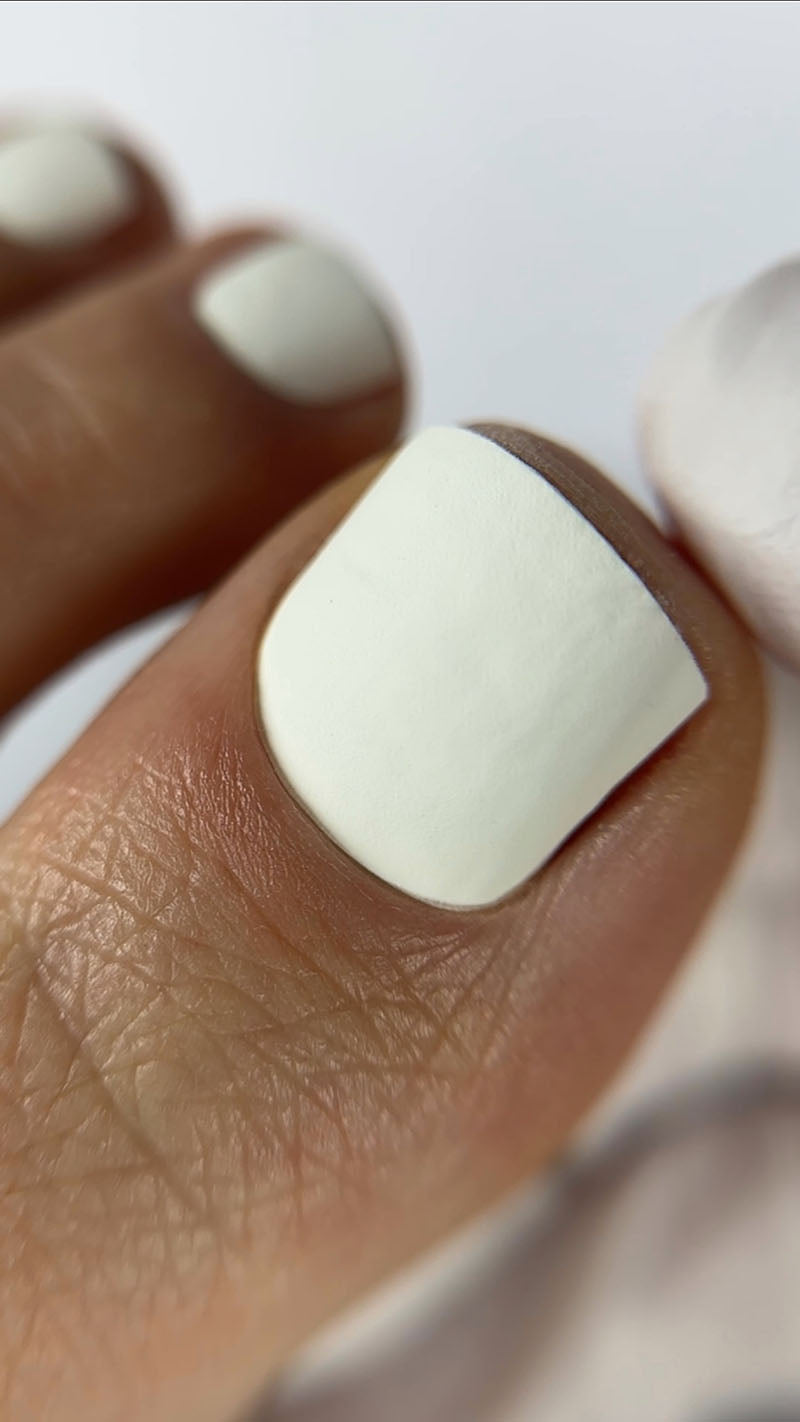 Close-up of a hand with white nail polish on a neutral background