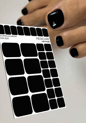 Sheet of black nail wraps held by a hand with black nail polish on a light gray background
