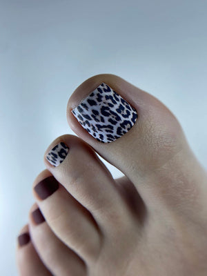 Close-up of a foot with leopard print nail polish on a plain background