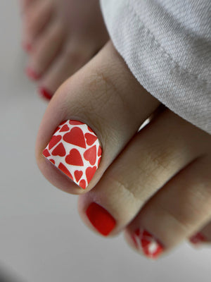 Close-up of toes with red heart nail design on a neutral background