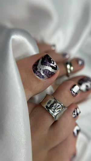 Close-up of a hand with silver and purple nail design on a white fabric background