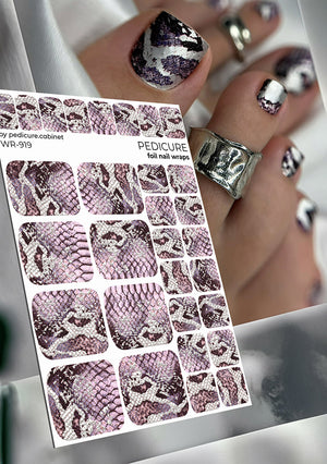 Sheet of nail foil wraps with snake pattern design, held by a hand with silver and black nail art.