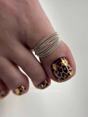 Close-up of a hand with leopard print nail design and silver ring on a neutral background