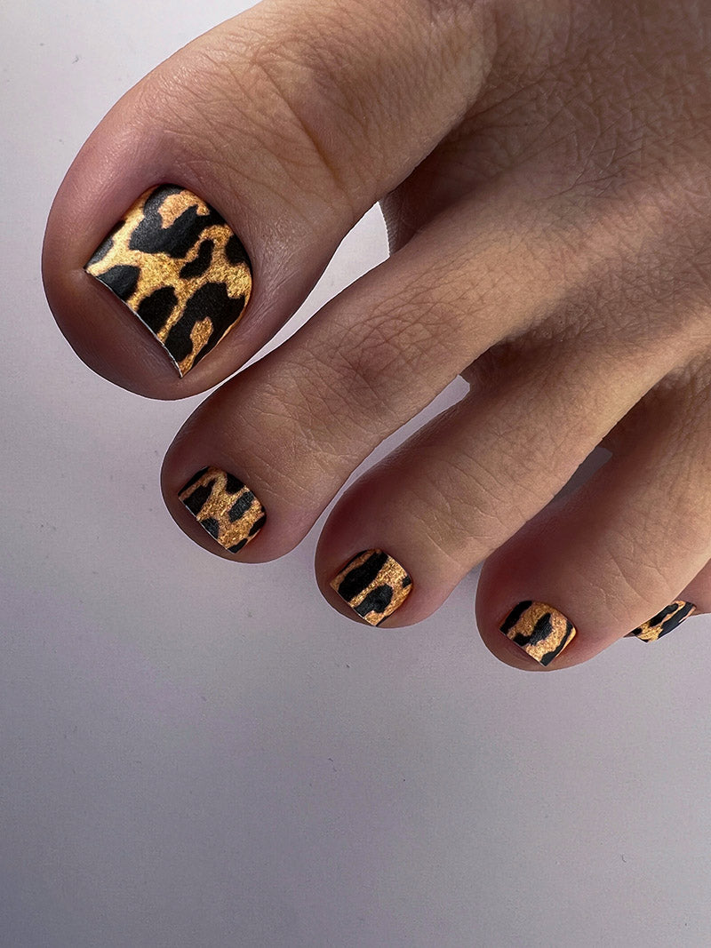 Toes with leopard print nail design on a plain background