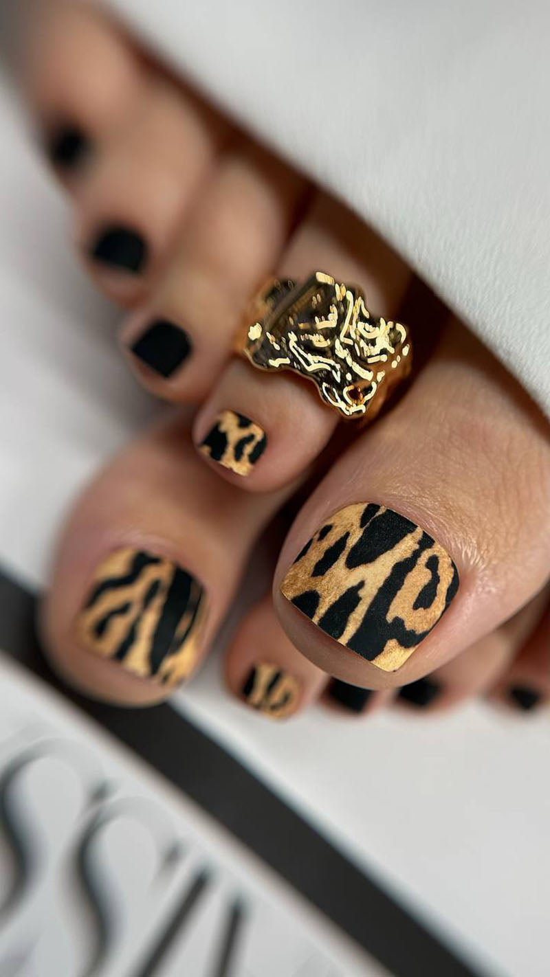 Nails with leopard print design and gold ring on a neutral background