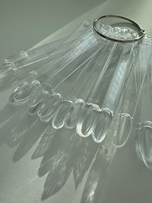 A collection of transparent, oval-shaped nail art tips laid out on a surface, with a metal ring for attachment.