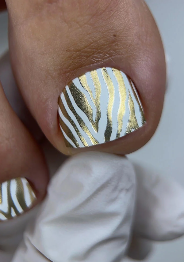 Nail with gold and white striped design on a neutral background