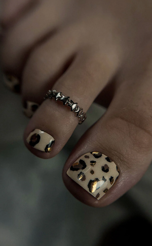 Close-up of toes with gold nail polish and a chain ring on a blurred background