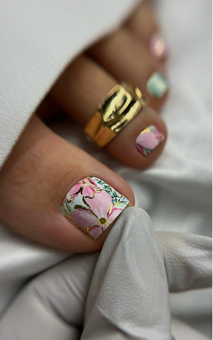 Close-up of a hand with floral nail art wearing a gold ring.