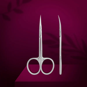 A pair of professional cuticle scissors with curved blades, displayed against a purple background with a magnolia leaf motif.