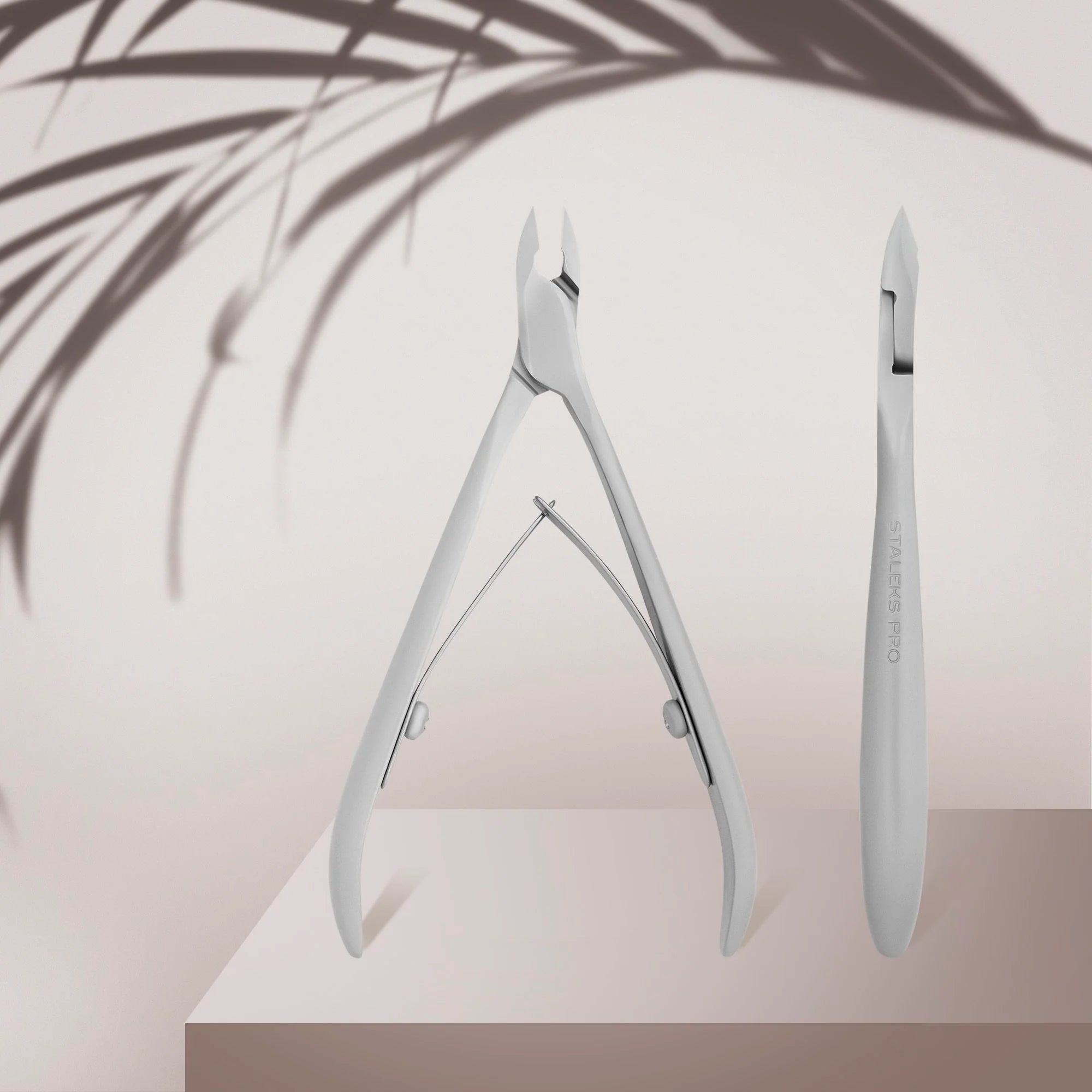A pair of professional cuticle nippers with straight cutting edges, shortened handles, and a satin finish, displayed against a neutral background.