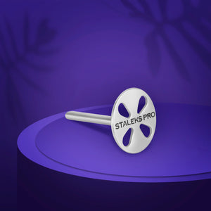 A metal pedicure disc with the brand name STALEKS PRO on it, displayed on a purple stand against a purple background.