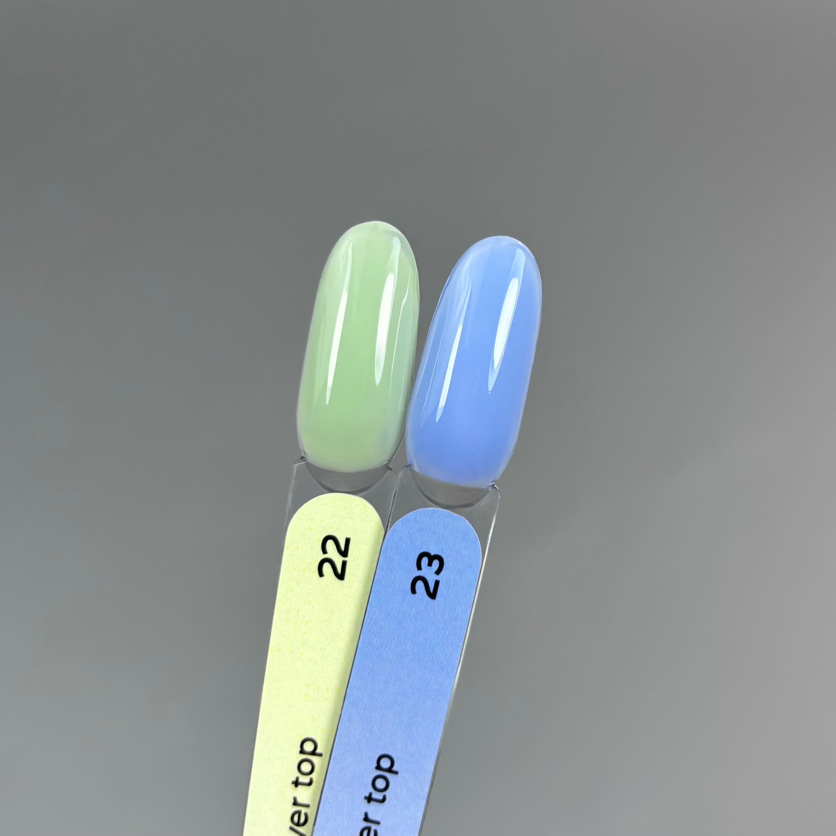 Two artificial nail tips swatched with polish colors 22 and 23 on a gradient gray background. Color 22 is a pale mint green, and color 23 is a soft sky blue.