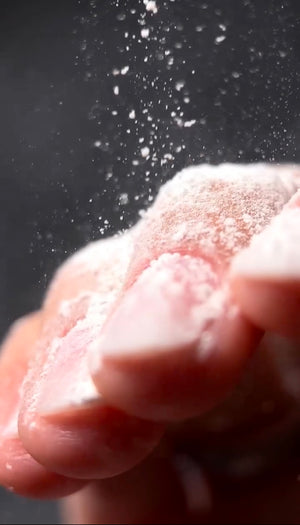 A close-up of a hand crushing or crushing with white powder suspended in the air against a dark background.