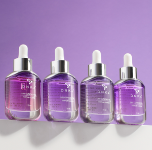 Four DNKA perfume flacons on a white surface with a purple background