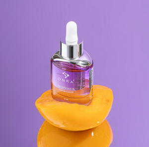 Bottle of DNKA oil on a yellow fruit with a purple background