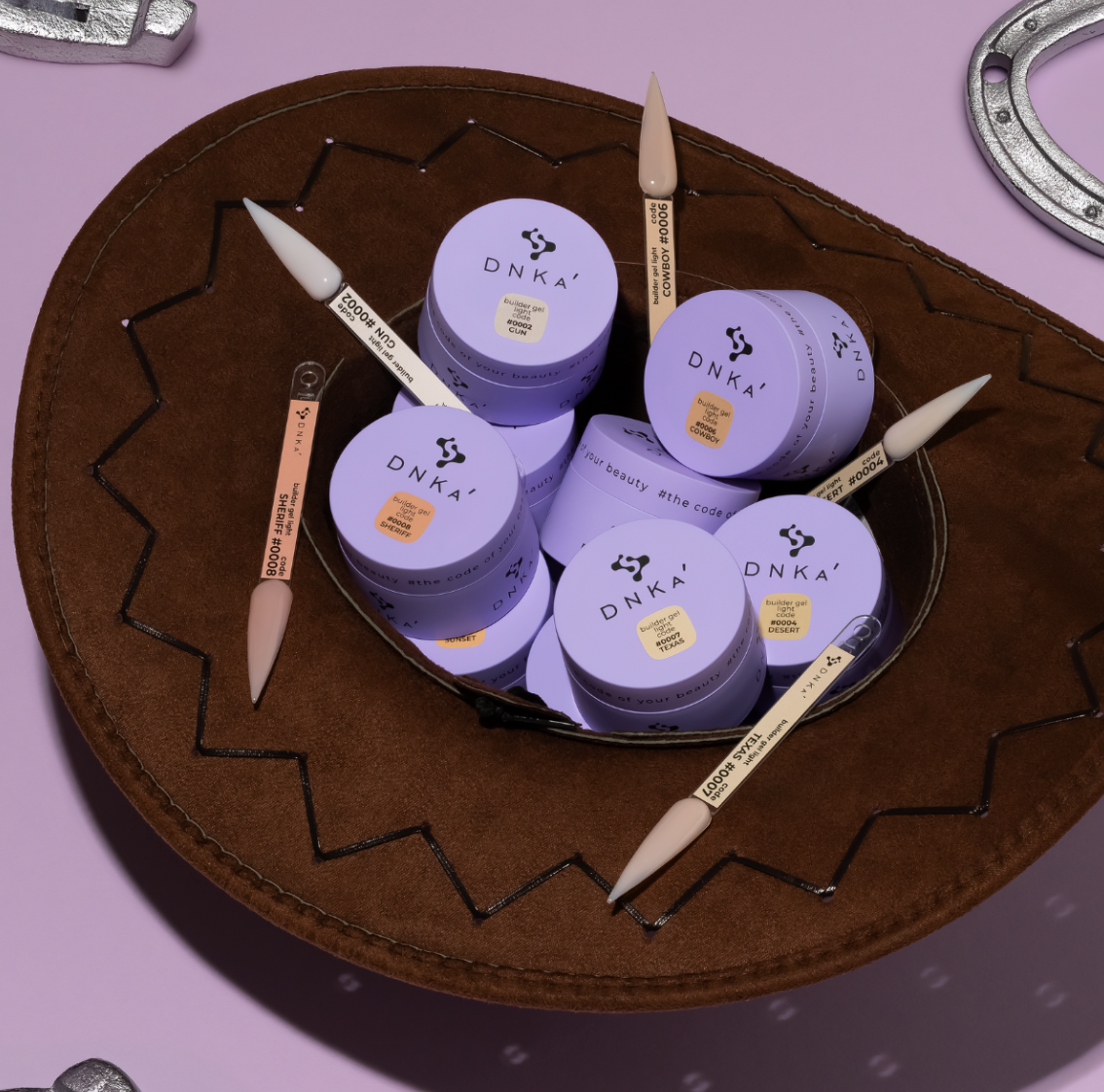 DNKA beauty products including jars and applicators on a decorative brown plate with a pink background.