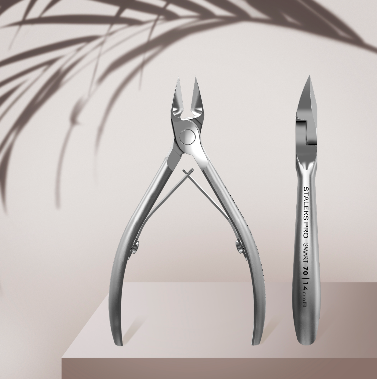 Pair of nail clippers on a light background with a palm leaf shadow