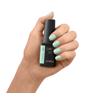 Hand holding a bottle of Kinetics nail polish with light green nails on a white background