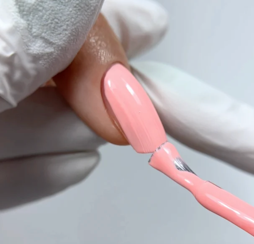 Close-up of a hand with pink nail polish applying another coat on a light gray background