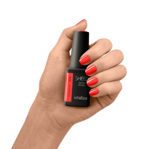 Hand holding a bottle of Kinetics nail polish with red nails on a white background